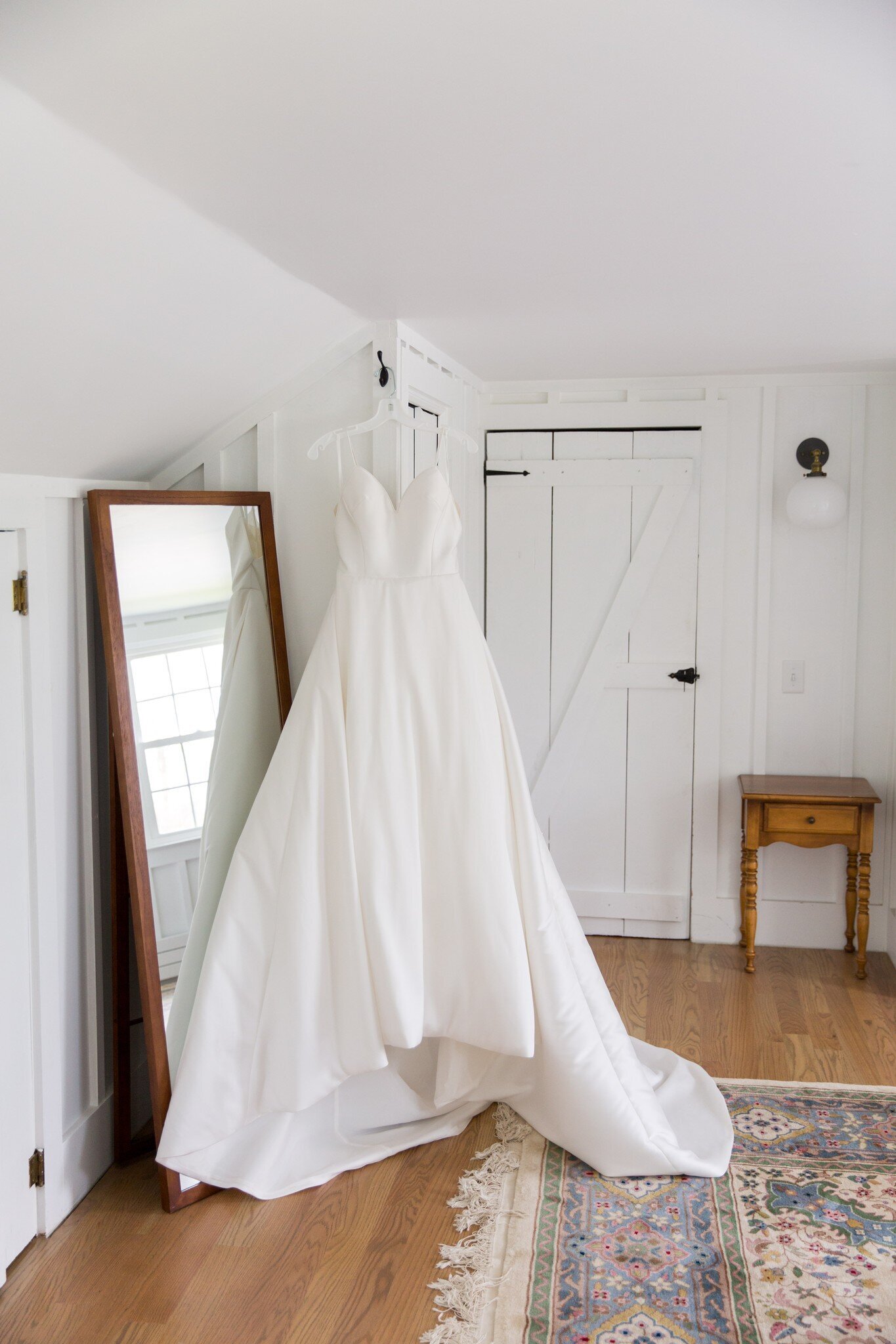 white bridal gown haninging in newlywed suite next to a floor length mirror and vintage rug Upstate
