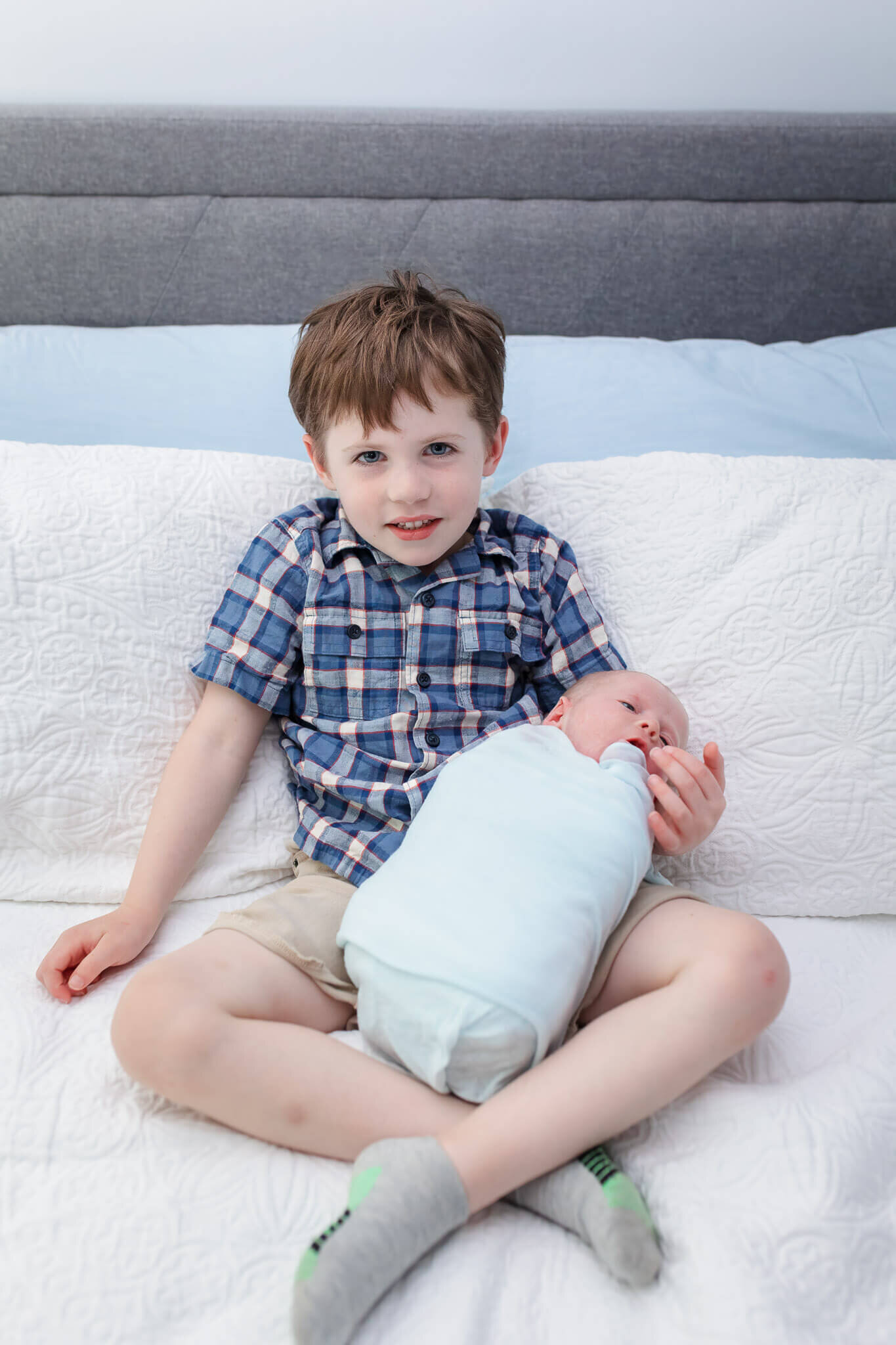 A big brother holding his newborn brother in bed.