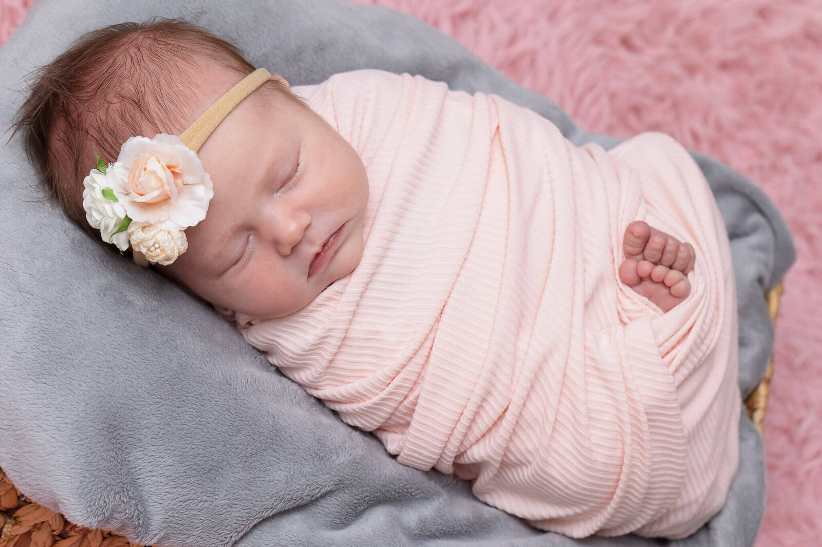 A newborn girl wrapped in pink laying in a basket with a gray blanket.