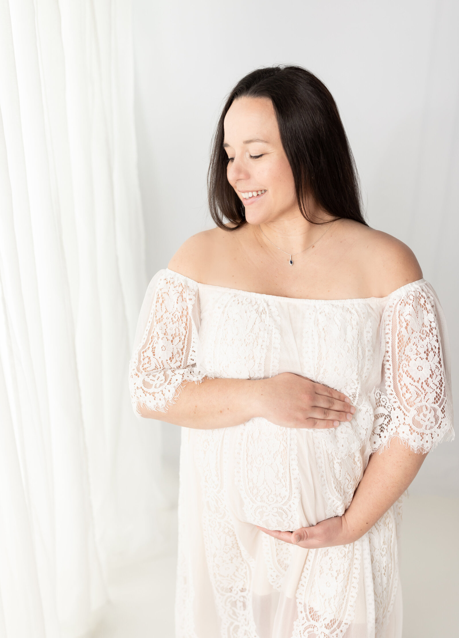pregnant mother in white lace dress holding belly for maternity photos cleveland maternity photographer