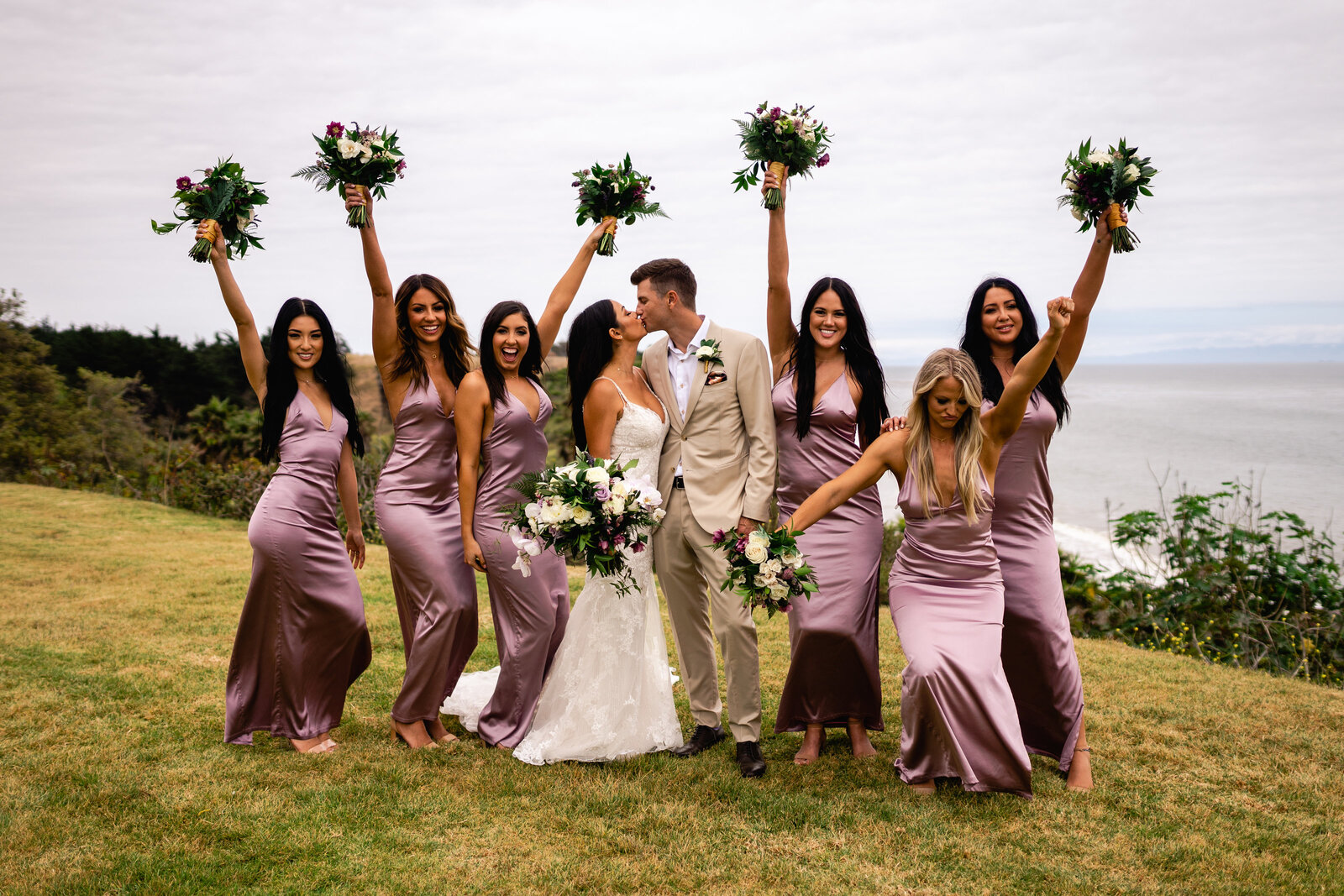 Wedding couple kissing with bridal party around them throwing their arms around being really excited.