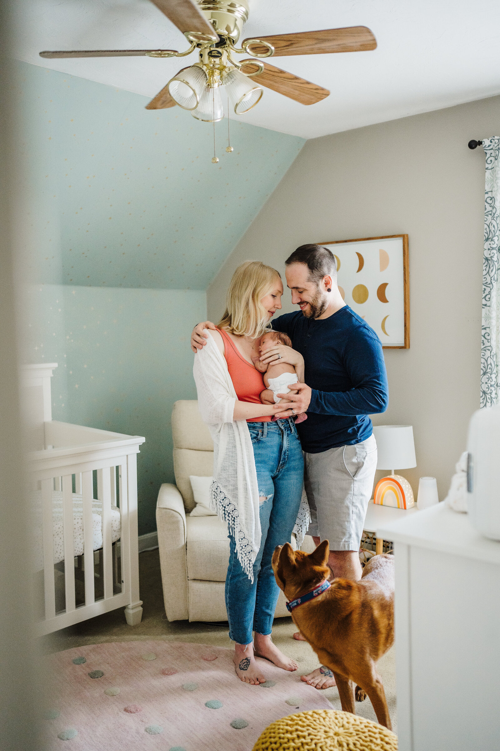 new parents stand with baby and dog in moon themed nursery