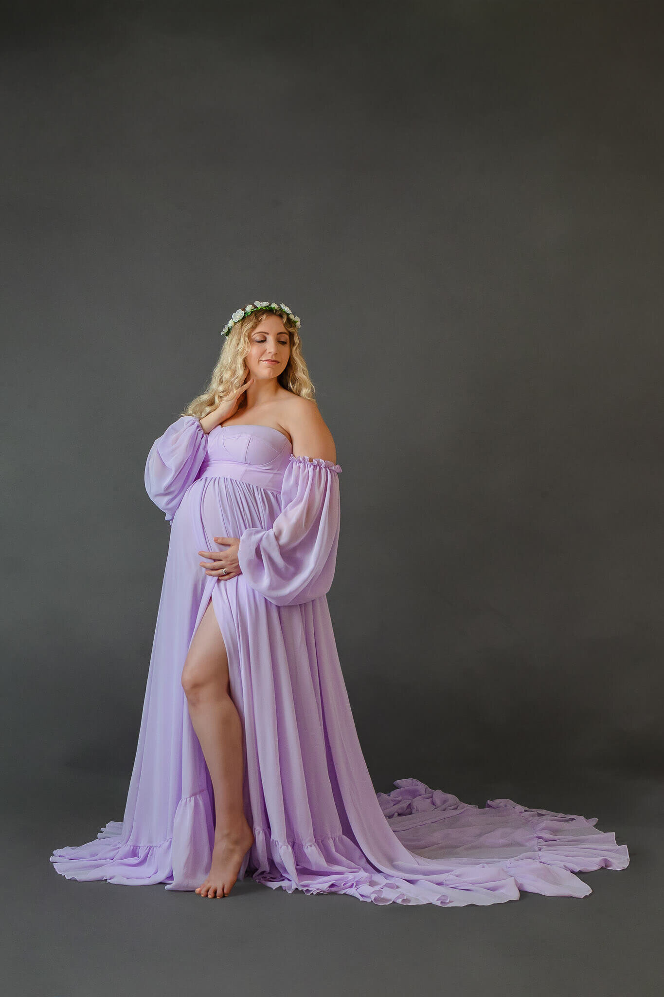 A mother-to-be in a purple dress holding her belly and showing off her leg through a slit.