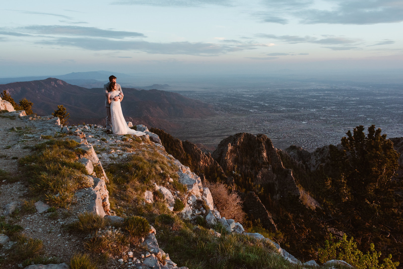 Wedding couples walks above a waterfall streaming down a grassy mountainside.