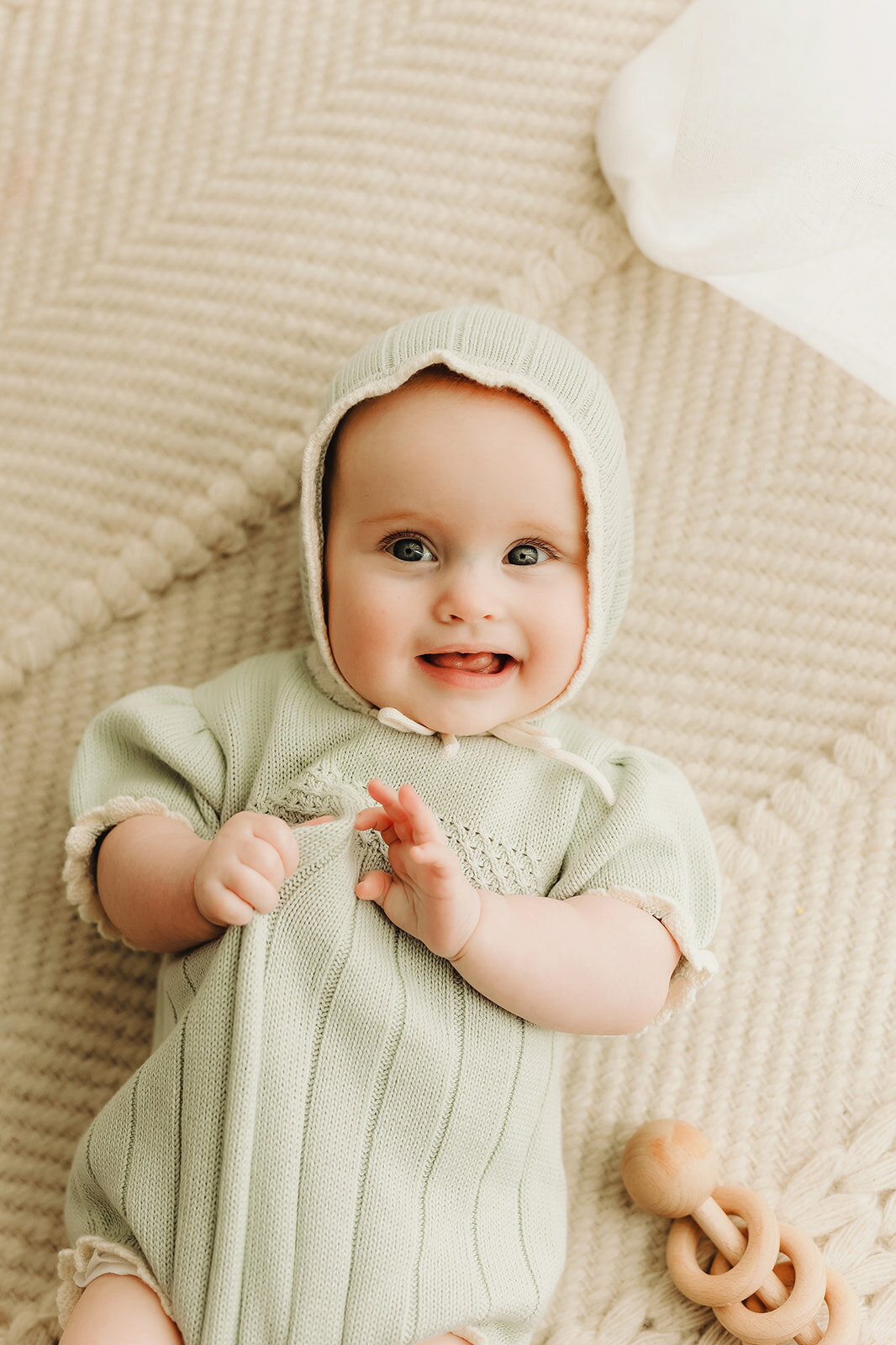 a 3 month old baby lies on a neutral cream colored rug smiling at the camera inside a Vancouver Washington natural light photography studio