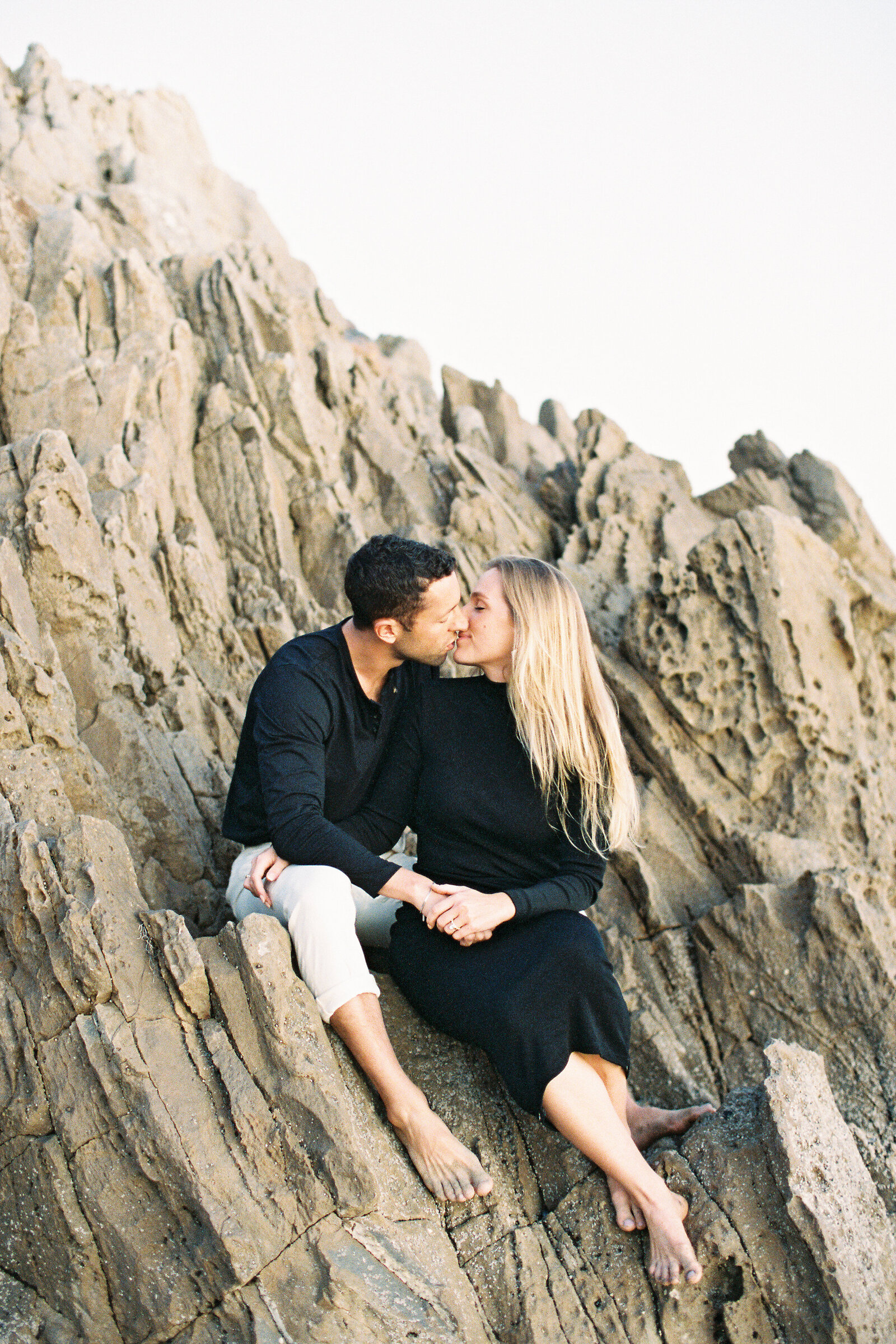 Couple sitting on rocks kissing each other.