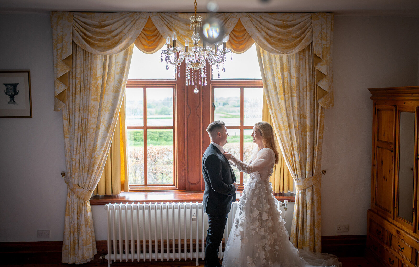 bride fixes groom's suit next to window