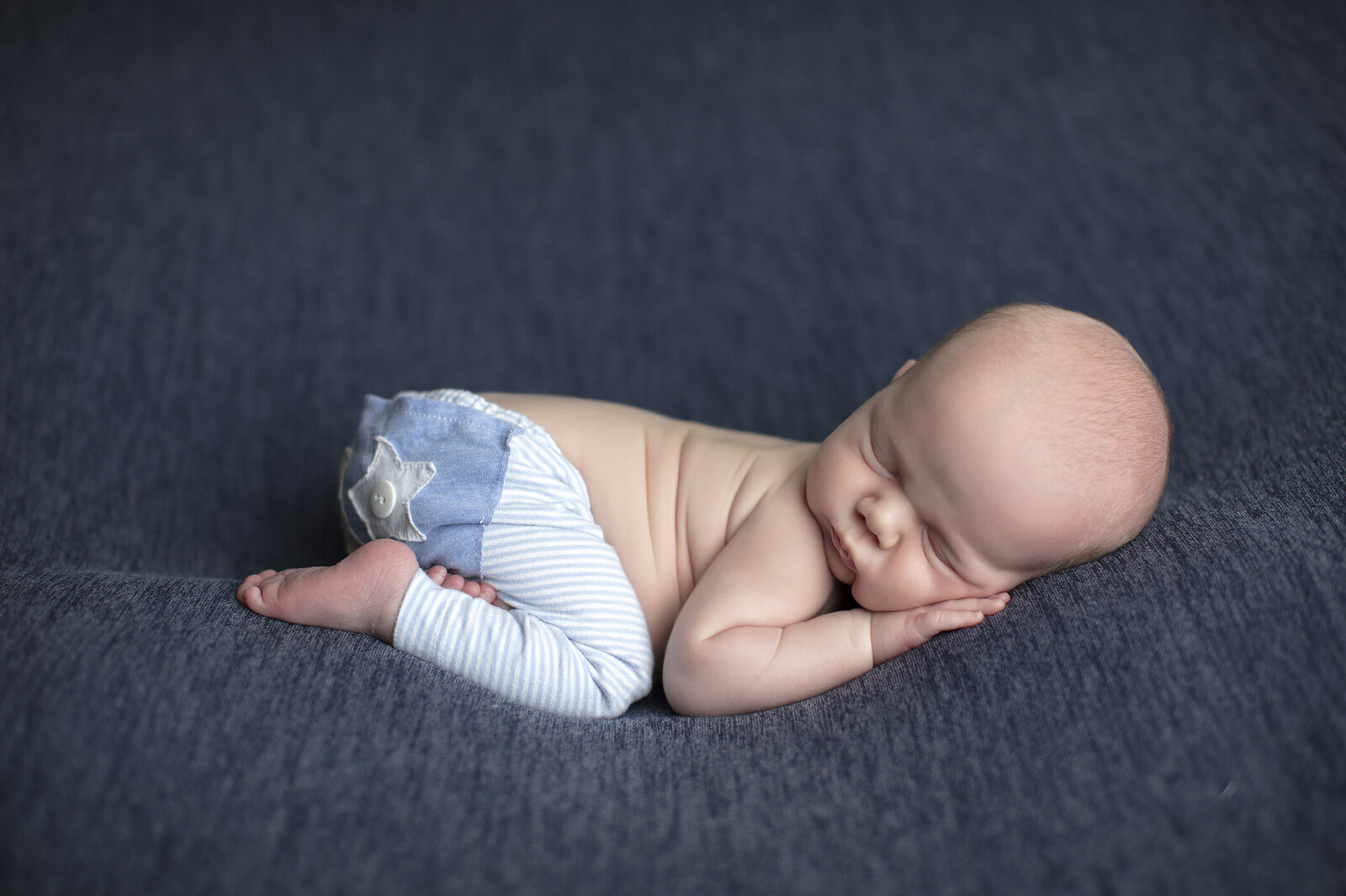 Newborn boy on blue fabric.