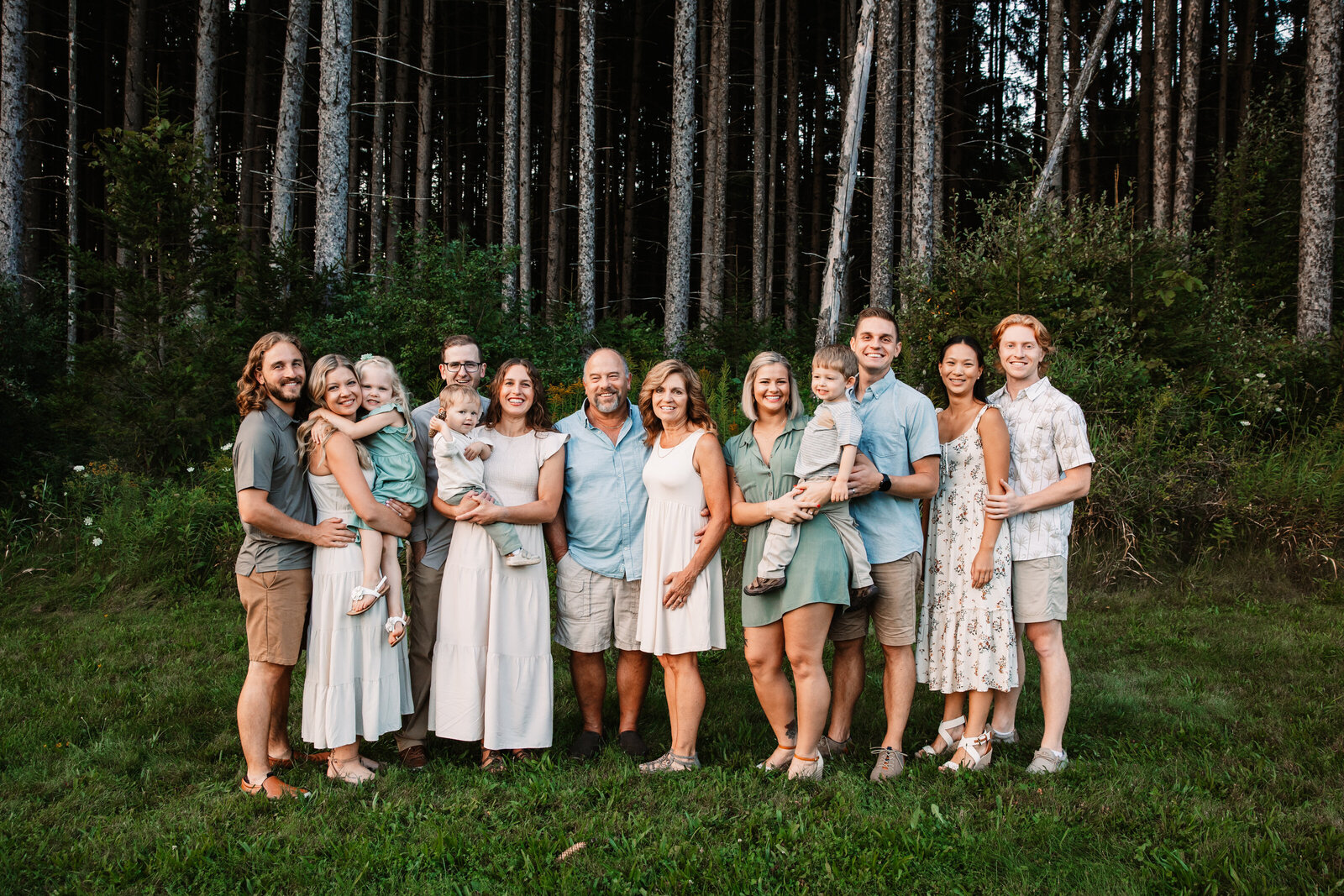 A large extended family stands on the edge of a field at sunset smiling