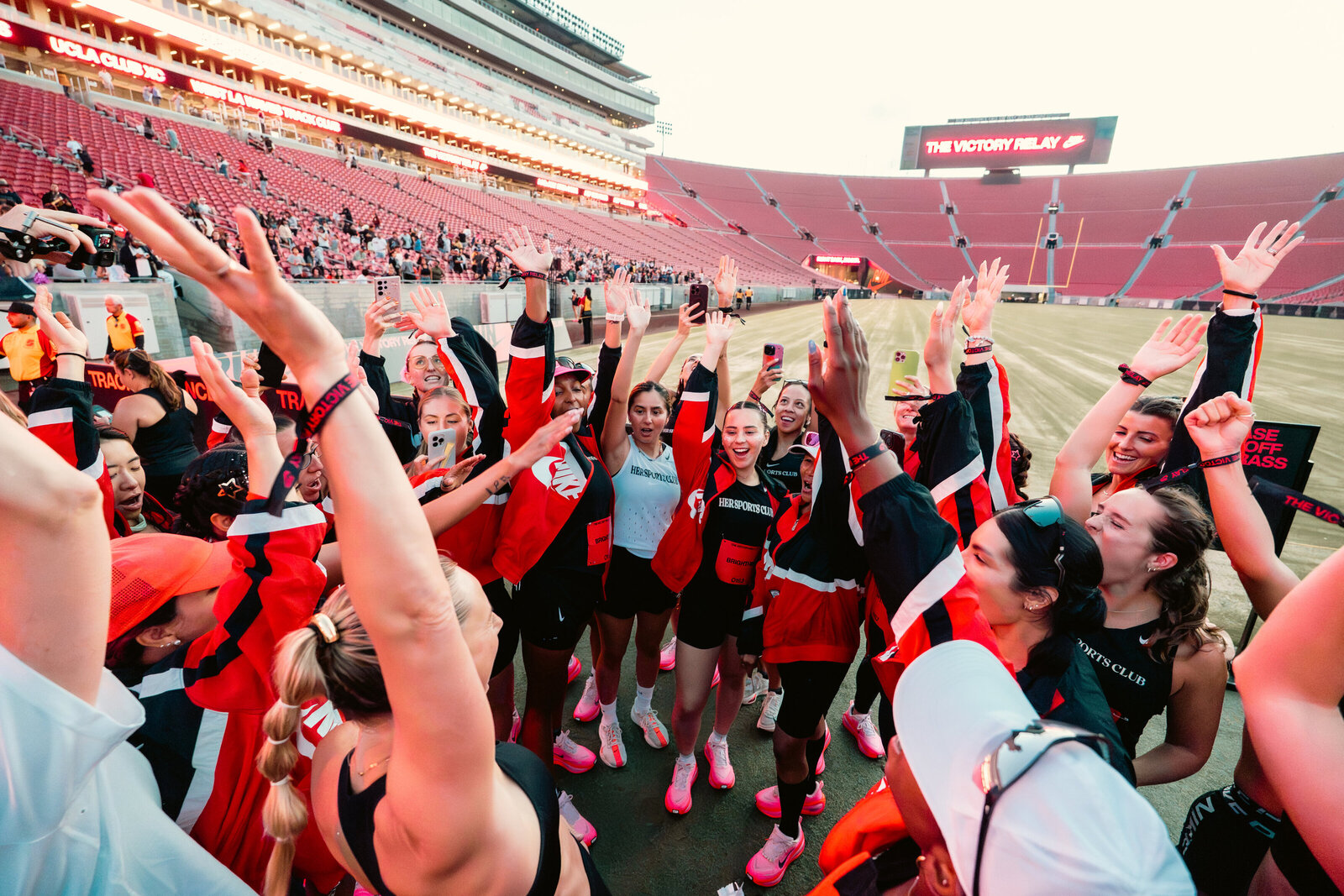 HER Sports Club team cheering together inside the stadium before a race.