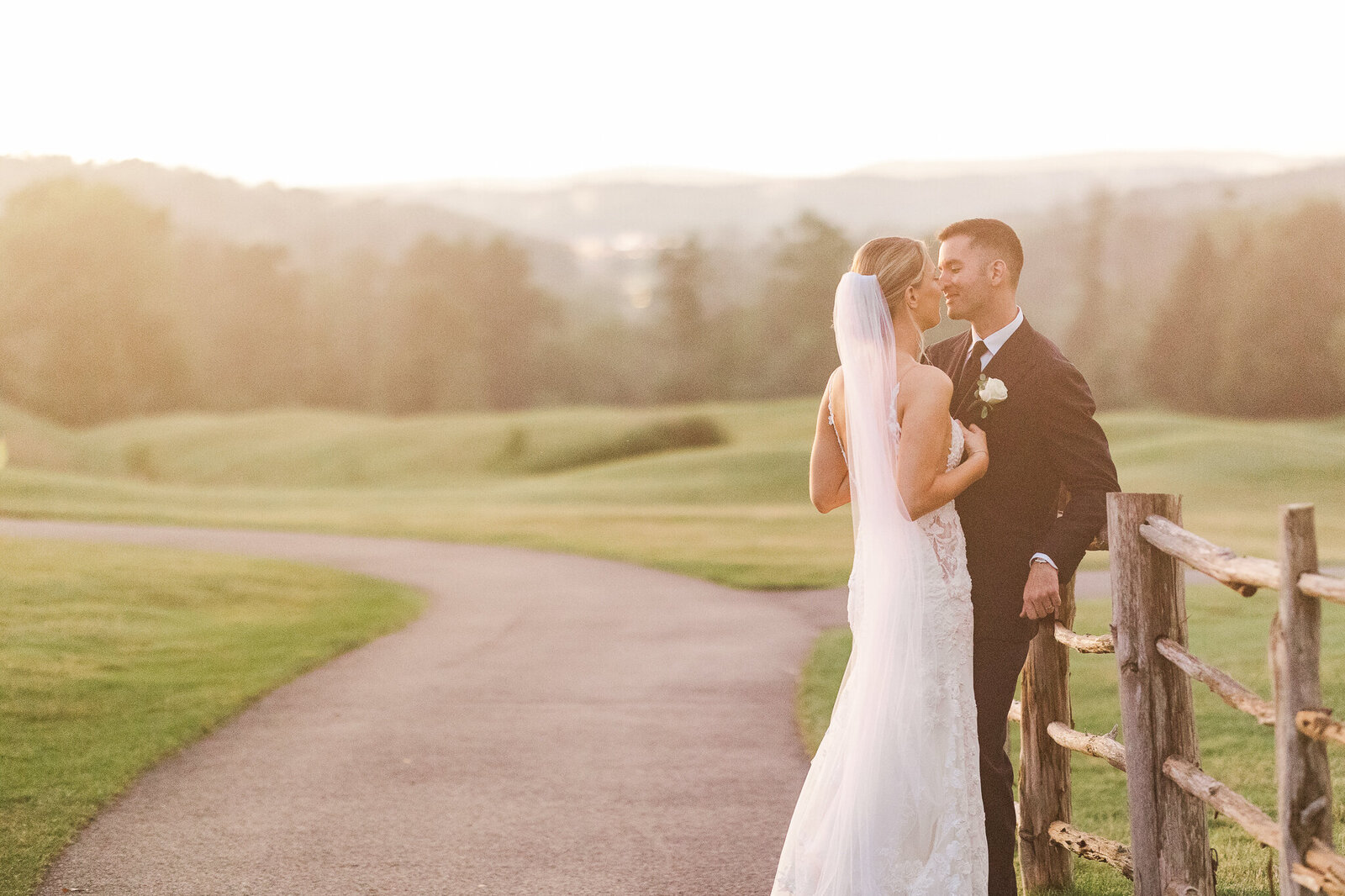 Bride leaning into groom on wooden fence during portraits at SkyView Golf Club