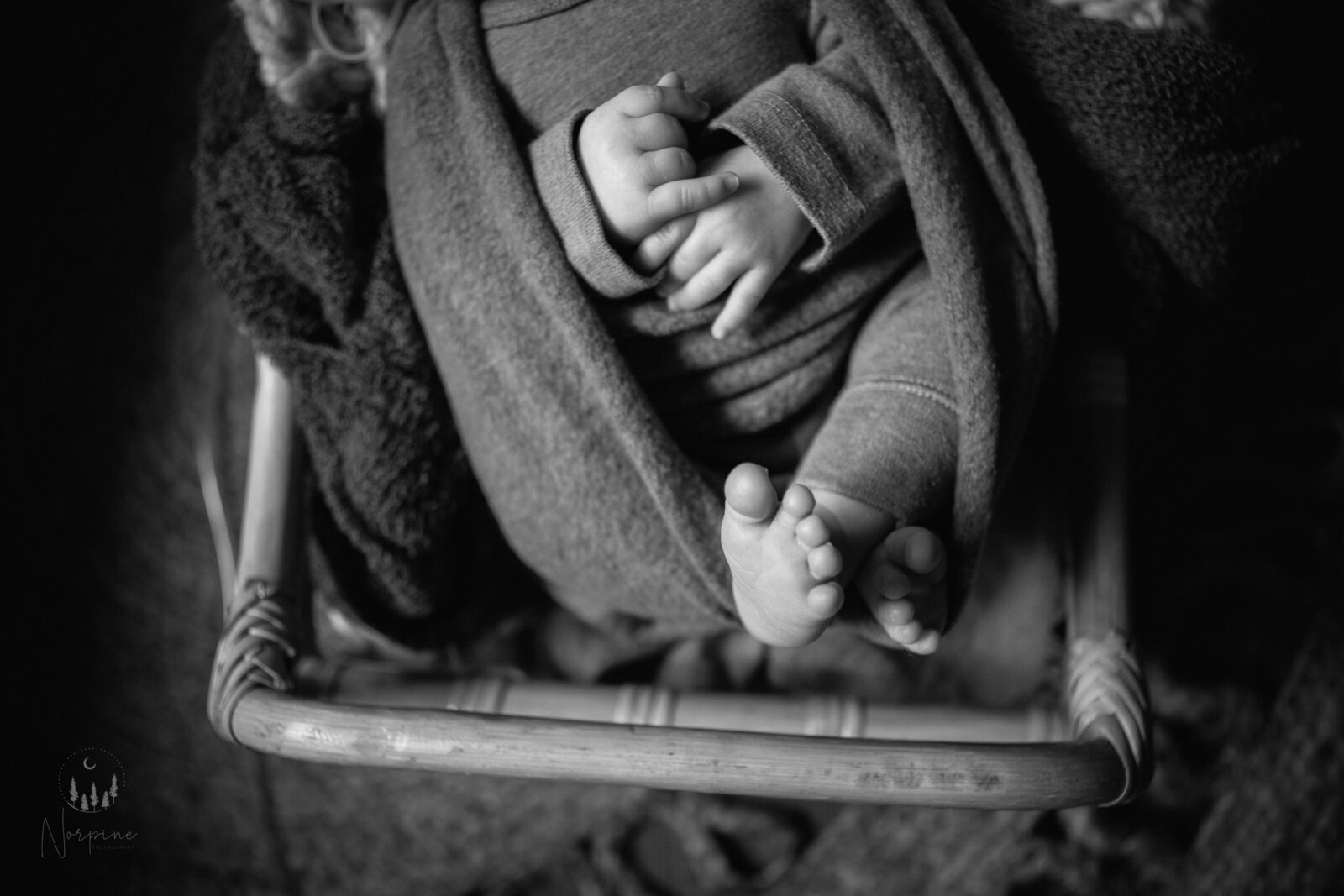 A black and white image of a newborn wrapped in a rattan bed with the focus on his hands and feet