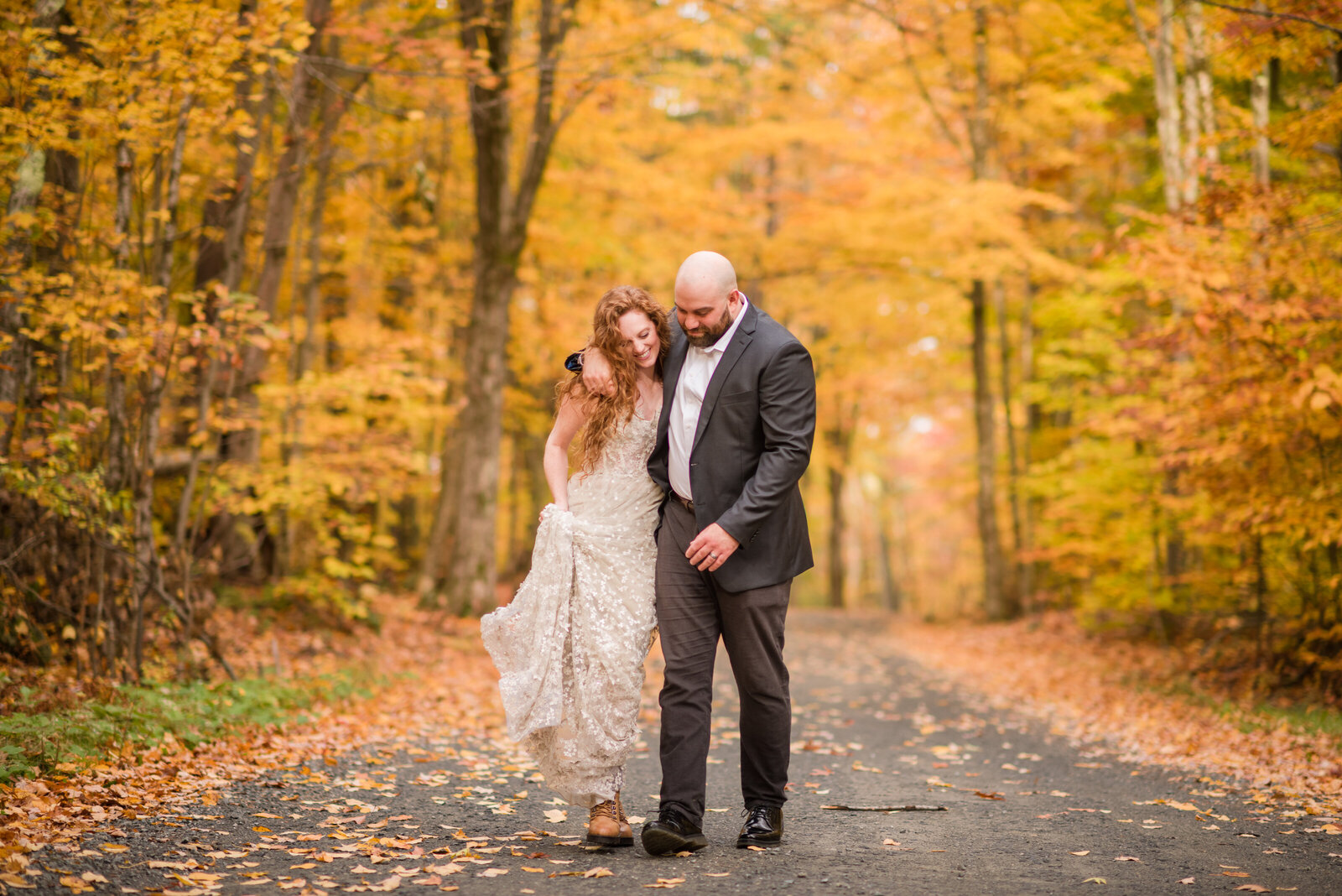 bride and her groom walking down a pathway with golden foliage toward their ceremony location.