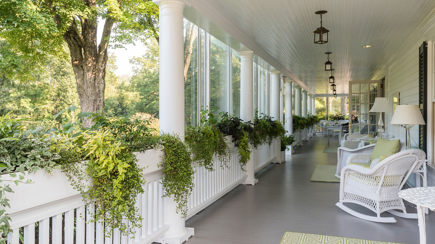 Porch with white rocking chairs and greenery hanging from railings