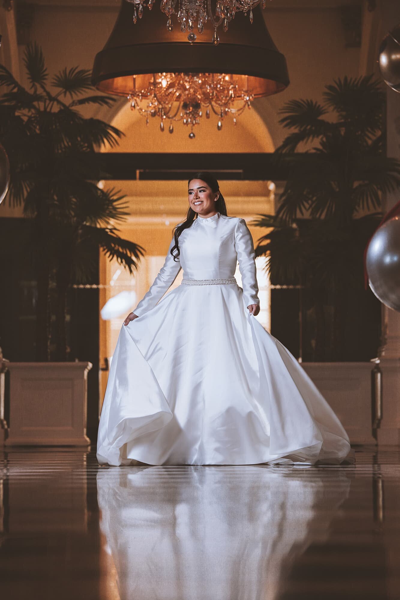 Elegant bridal portrait at Grand Galvez in Galveston, TX, featuring a bride in a timeless satin gown with long sleeves and a crystal belt, captured by luxury wedding photographer Logrono & Co. Weddings.