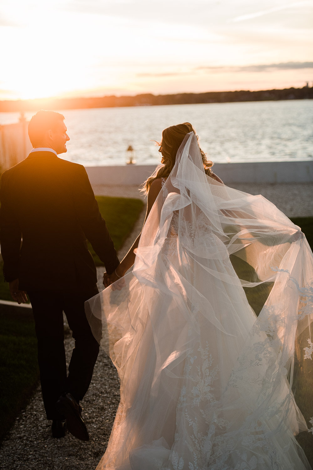 bride and groom walking towards water at sunset