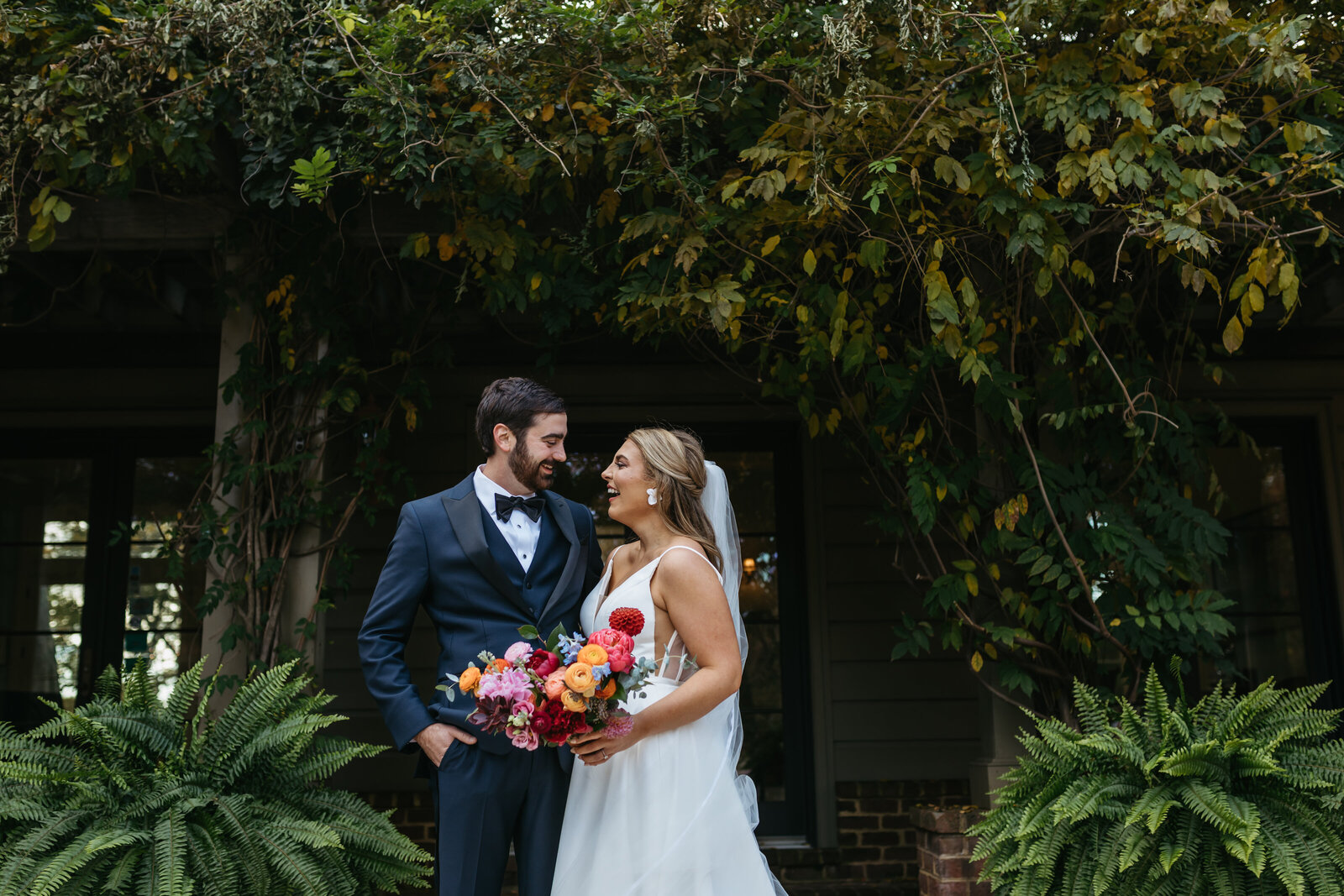 A bride and groom smile at each other under a canopy of leaves
