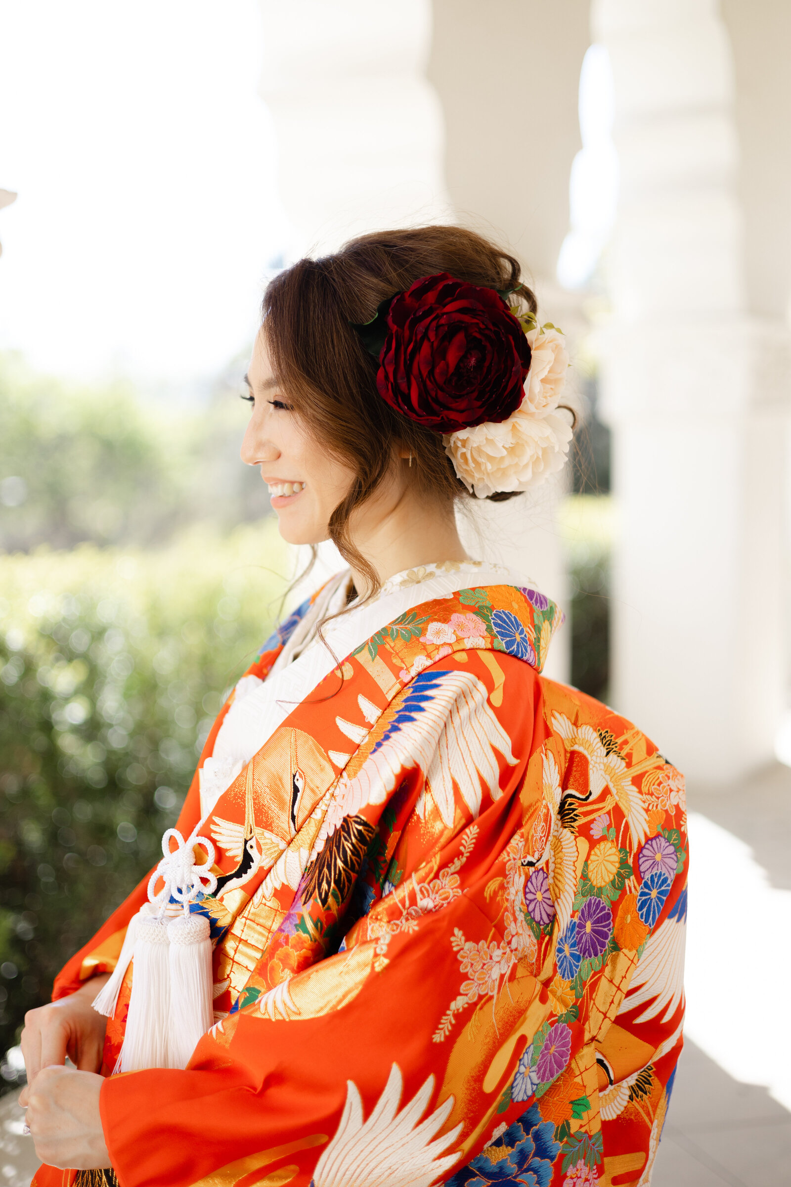 Bride in red iro uchikake wedding kimono with crane and floral motifs smiling softly at Brand Park Glendale, Los Angeles California. Perfect for wedding kimono rental | 赤い鶴と花の模様の色打掛をまといブランドパーク・グレンデールで優しく微笑む花嫁。ロサンゼルス カリフォルニアの和装ウェディング着物レンタル。