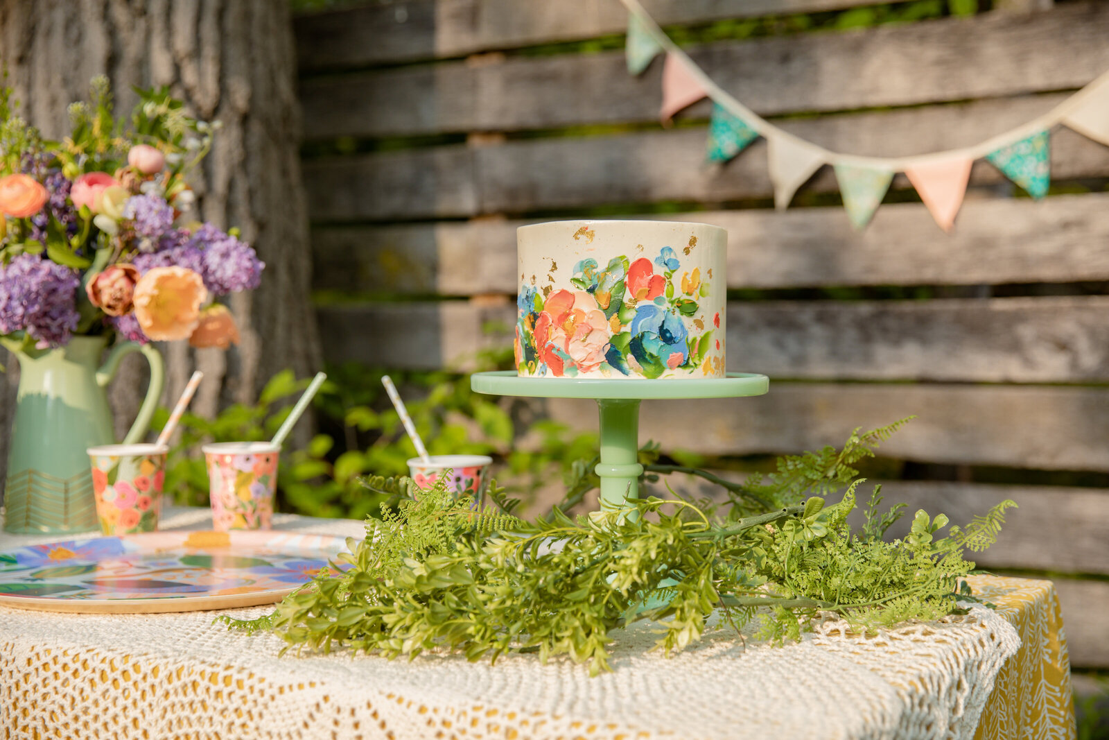 sweet heather ann garden party styled shoot with painted flower cake on green vintage cake stand with flowers in background