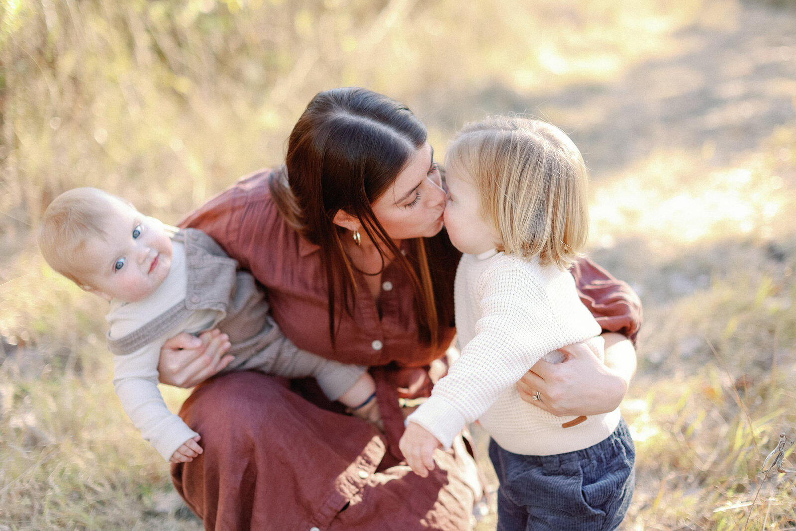 mom kissing her little boy while holding her baby boy