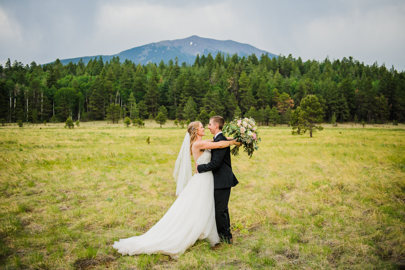 bride and groom looking at each other in field with pine trees and mountain views background in Flagstaff