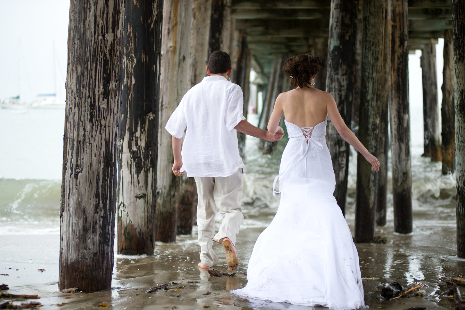 In beautiful beach engagement session, the couple walks under the pier in northern california