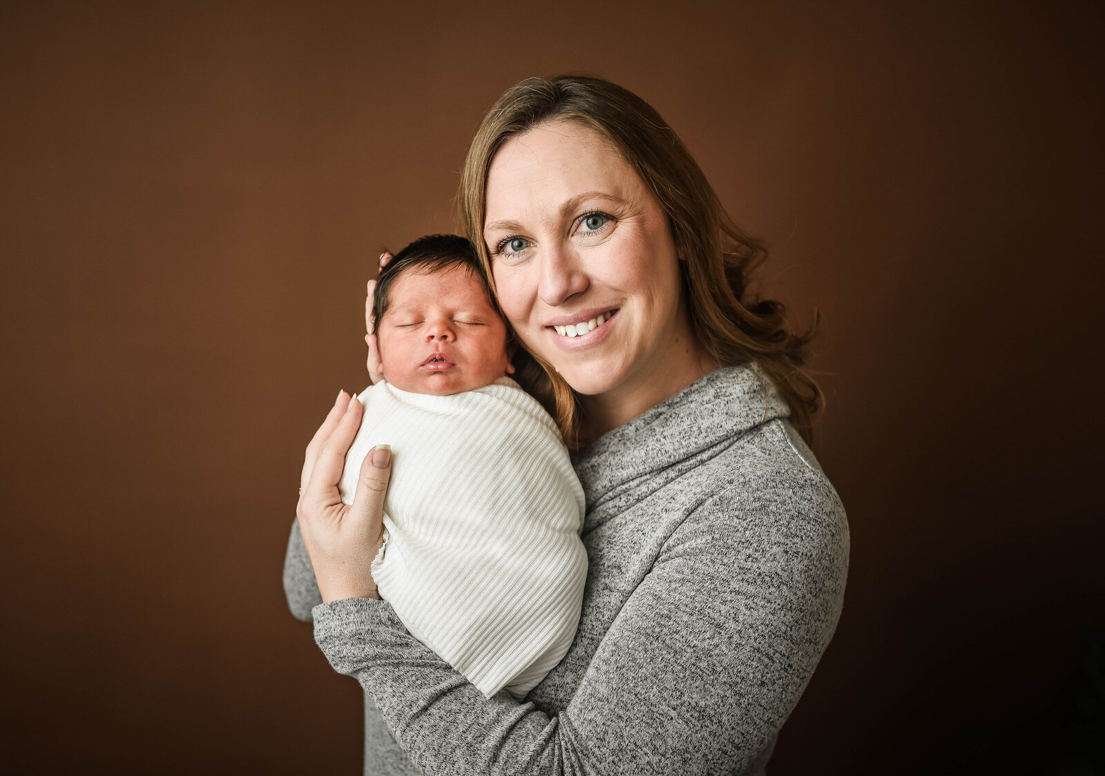 mother holding her newborn baby wrapped in swaddling white blanket