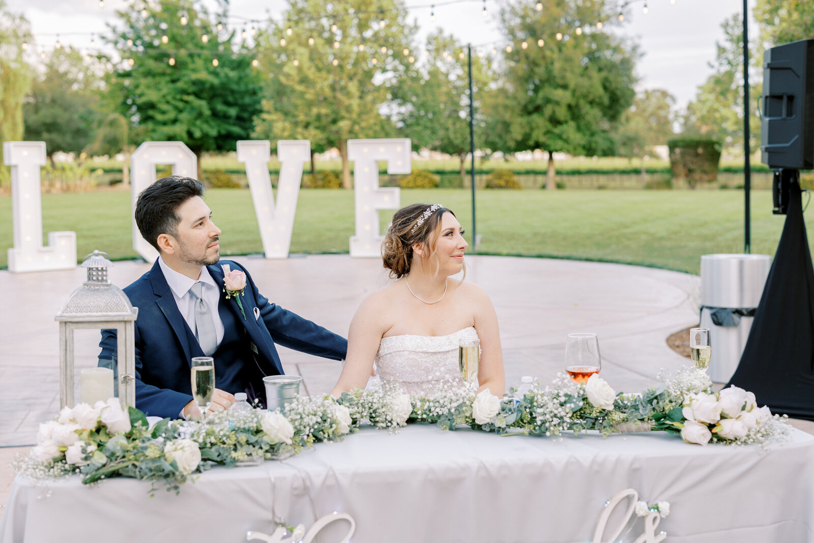 sacramento wedding photographer captures candid picture of bride and groom sitting together at their reception listening to toasts for their outdoor wedding reception