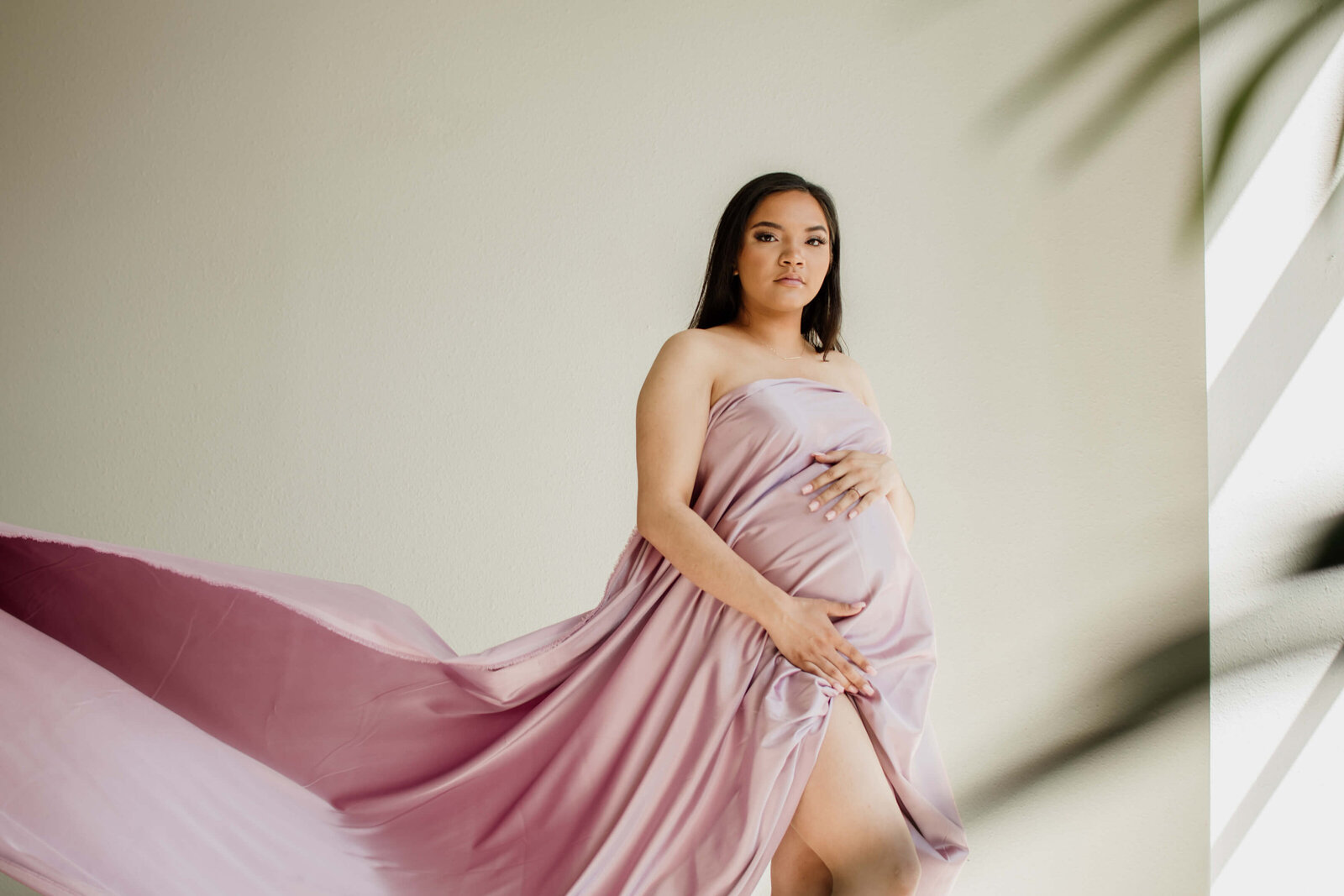 Pregnant woman holding pink satin fabric.