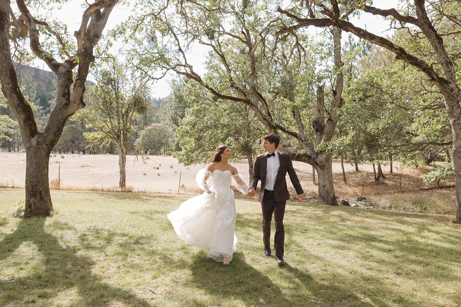 Bride twirling her dress while walking with the groom under the oak trees