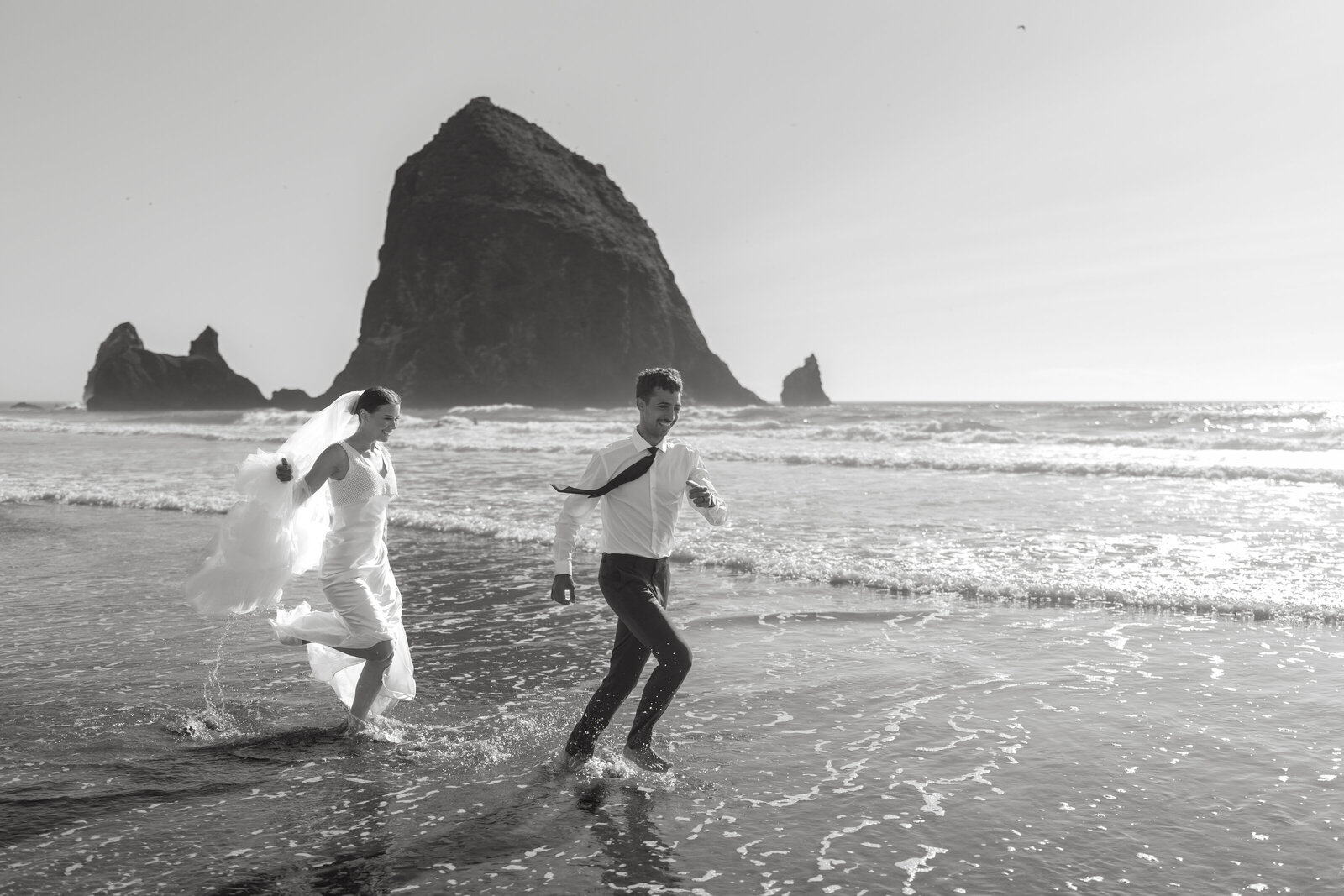 A bride and groom run around in front of the famous Haystack Rock at Cannon Beach after eloping there.