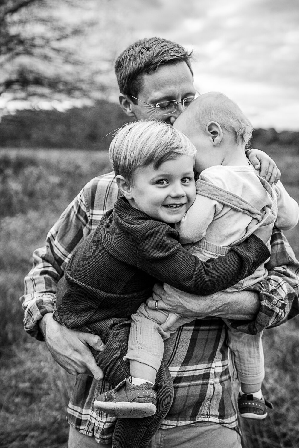 dad holds sons in hug while toddler boy looks at camera