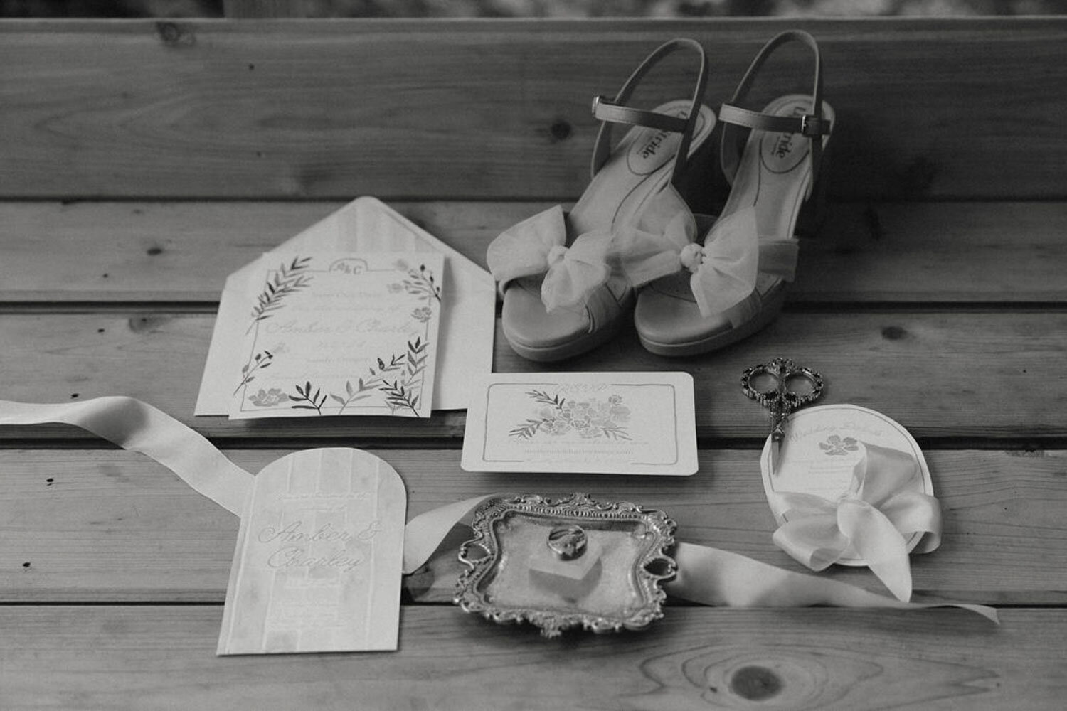 Black-and-white flat lay of wedding shoes, stationery, and ribbon