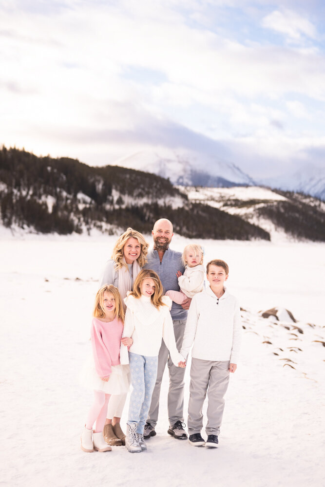 a family of 6 stands on a snowbank in the mountains