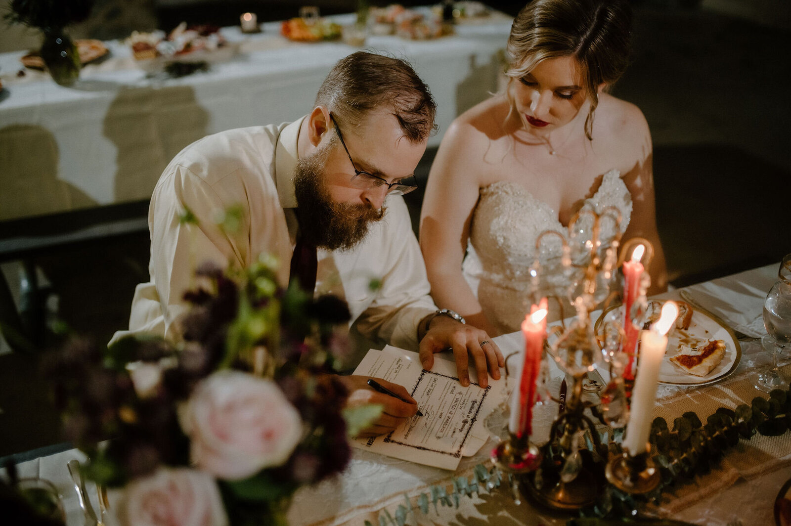 couple signing marriage license in candlelight at wedding reception table
