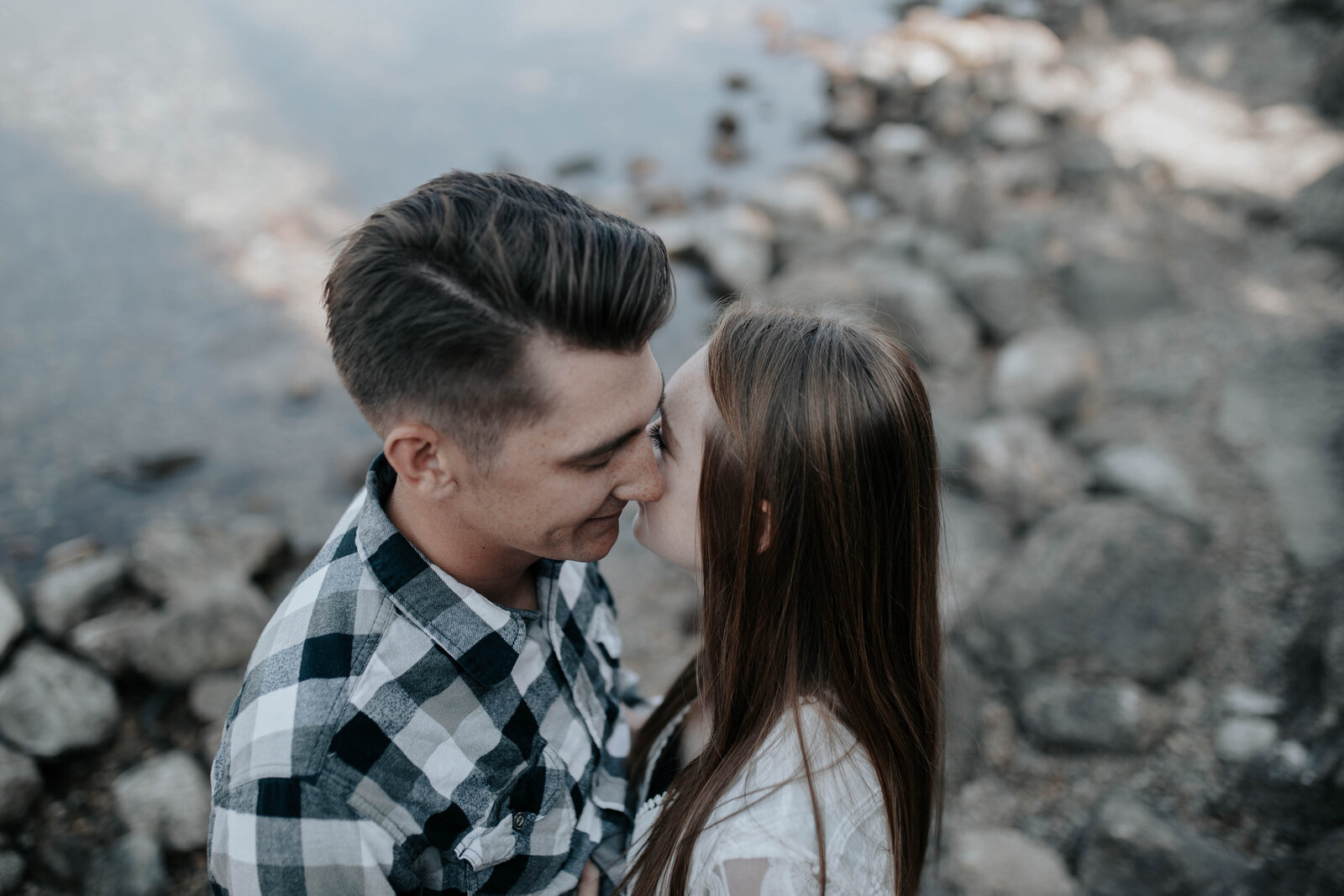 engagement photos at a lake with man and woman leaning in to kiss each other while smiling captured by Idaho Falls wedding photographer