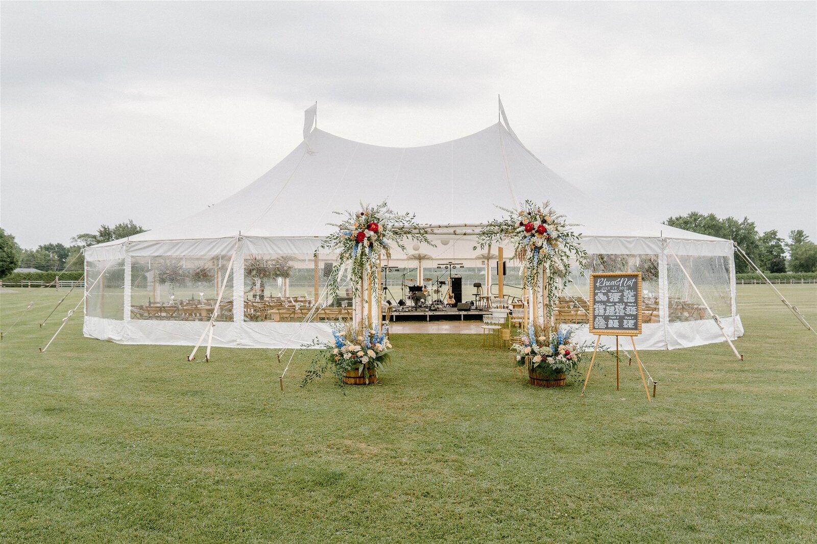 White Pole Tent with lush floral entrance set in a large green field Assorted Artistries Wedding Planning