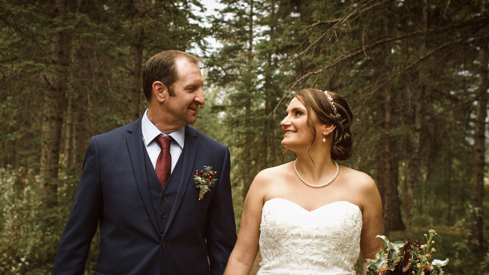 Couple walking down a trail during the filming of their wedding video in Canmore Alberta. Pictured smiling and enjoying their wedding day