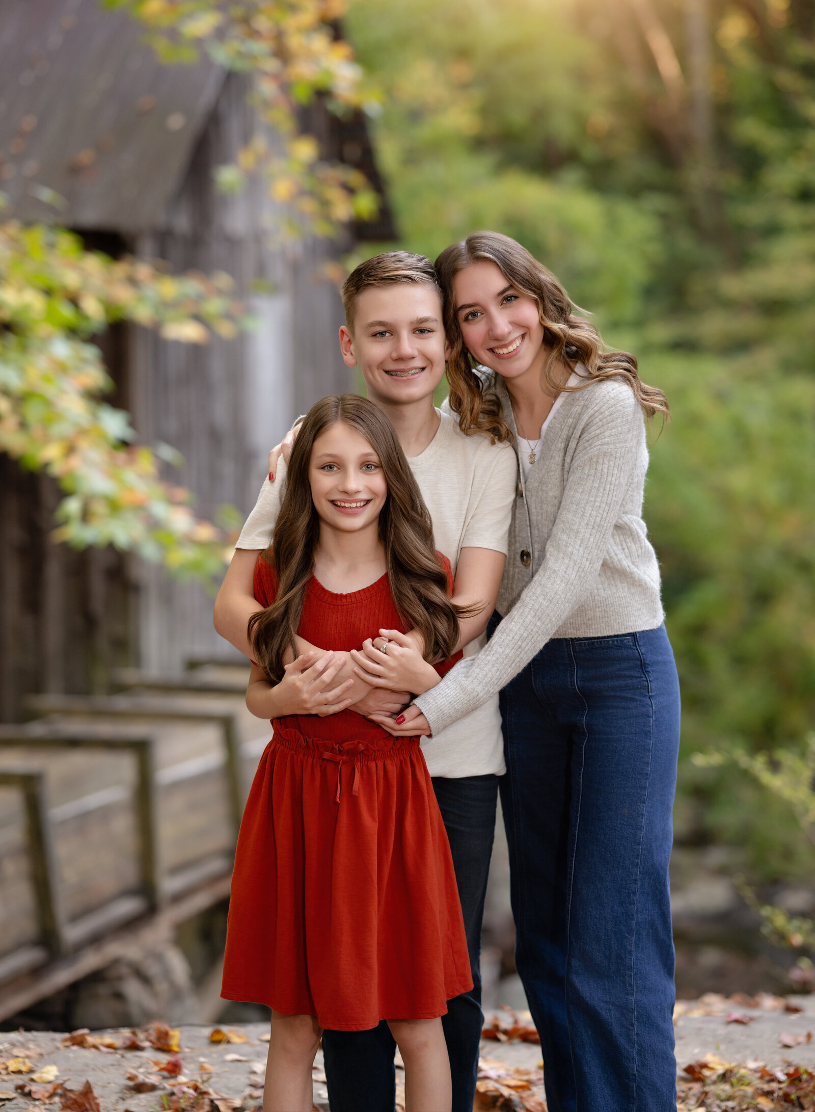 3 siblings hugging and smiling in the fall woods. Photo taken at Grist Mill in Marietta near Atlanta, GA.