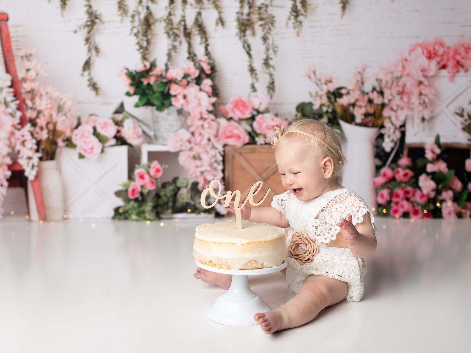 girl in white lace romper for first birthday cake smash