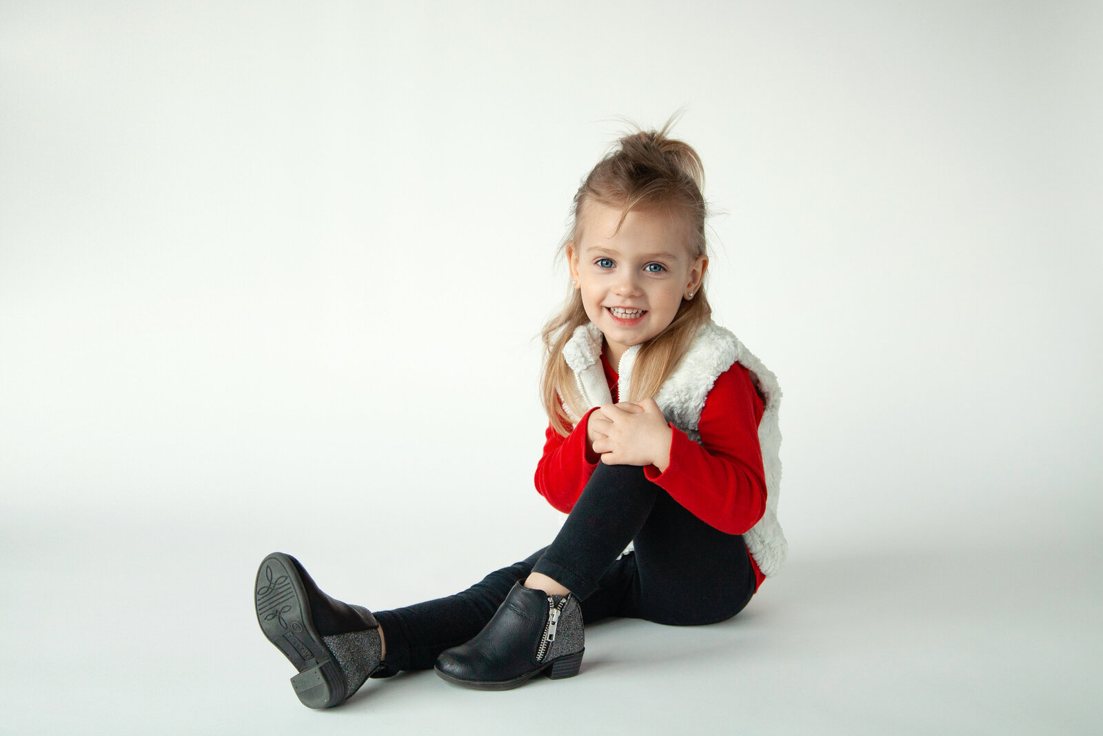 Young girl hugging her knee smiling in front of white background.