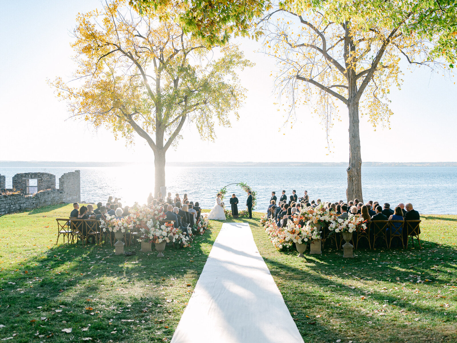 Wide photo of wedding ceremony on the lawn of Inns of Aurora with the Finger Lakes in the background.