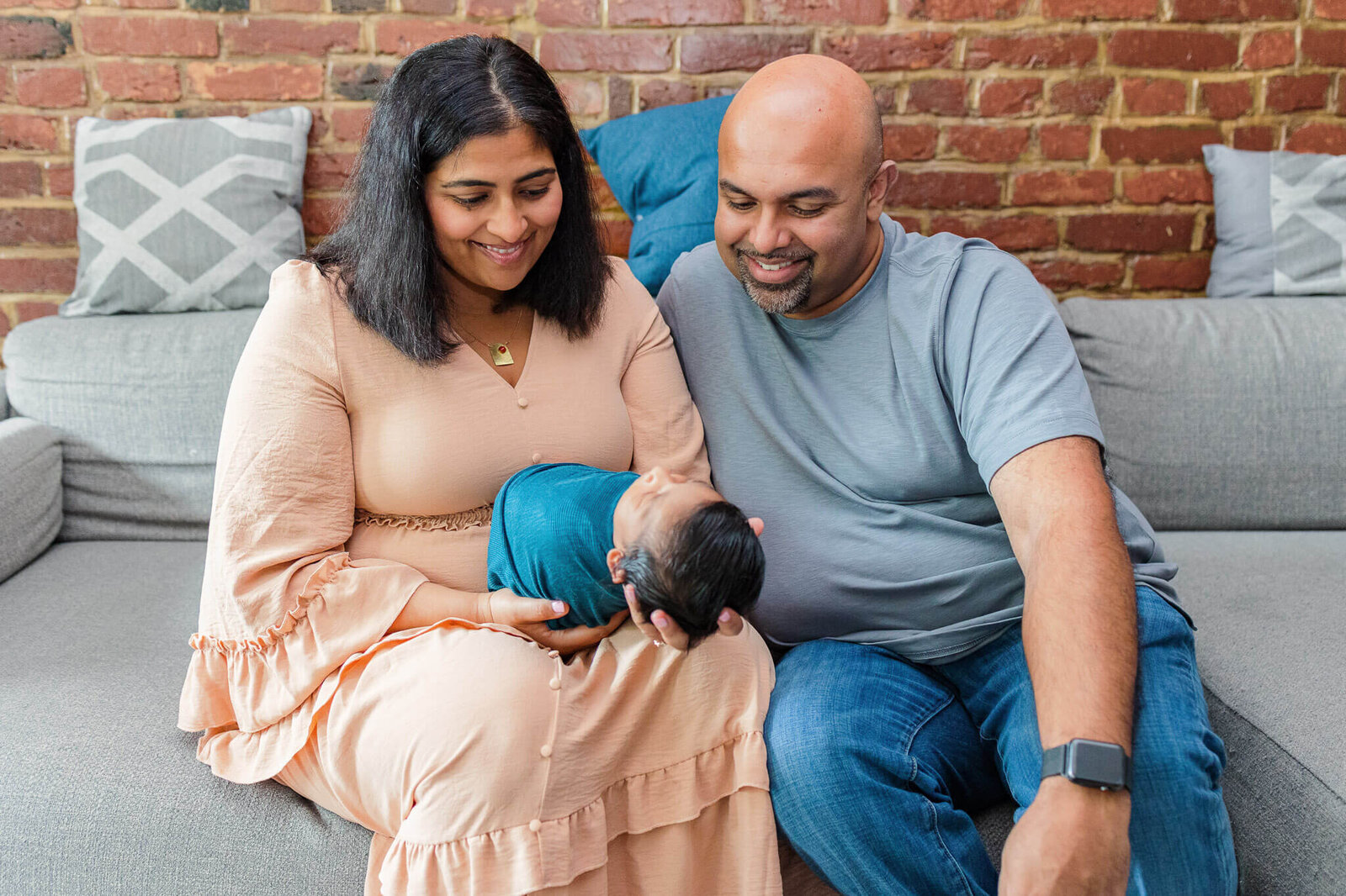 A couple sitting on the couch and holding their newborn son.