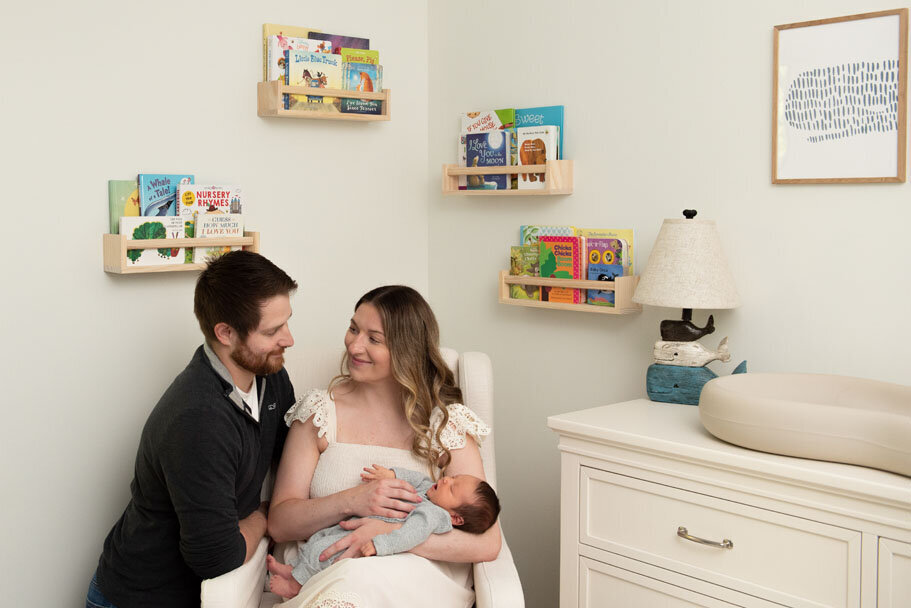Mom and dad rocking newborn in the nursery rocking chair with books on wall