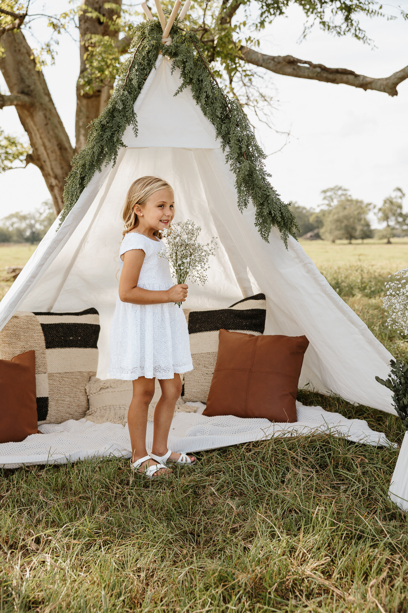Little girl standing with flowers during a teepee session in a farm field in Aiken Sc, surrounded by boho decor.