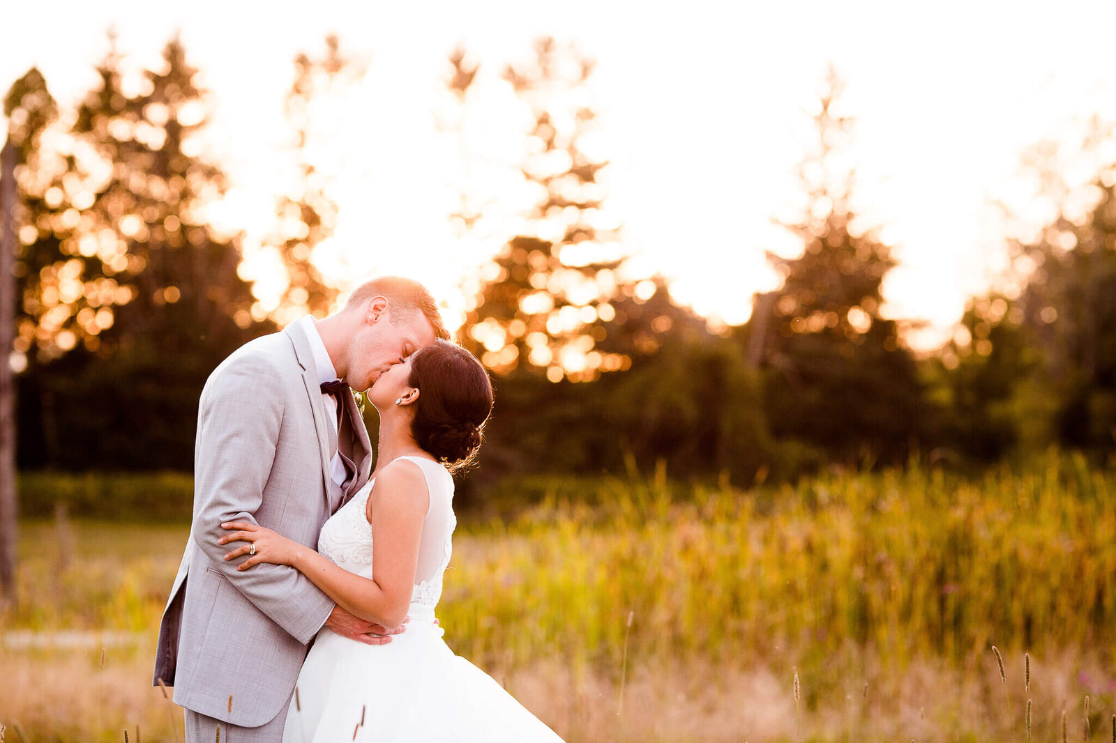 Bride and groom kiss in field at sunset.