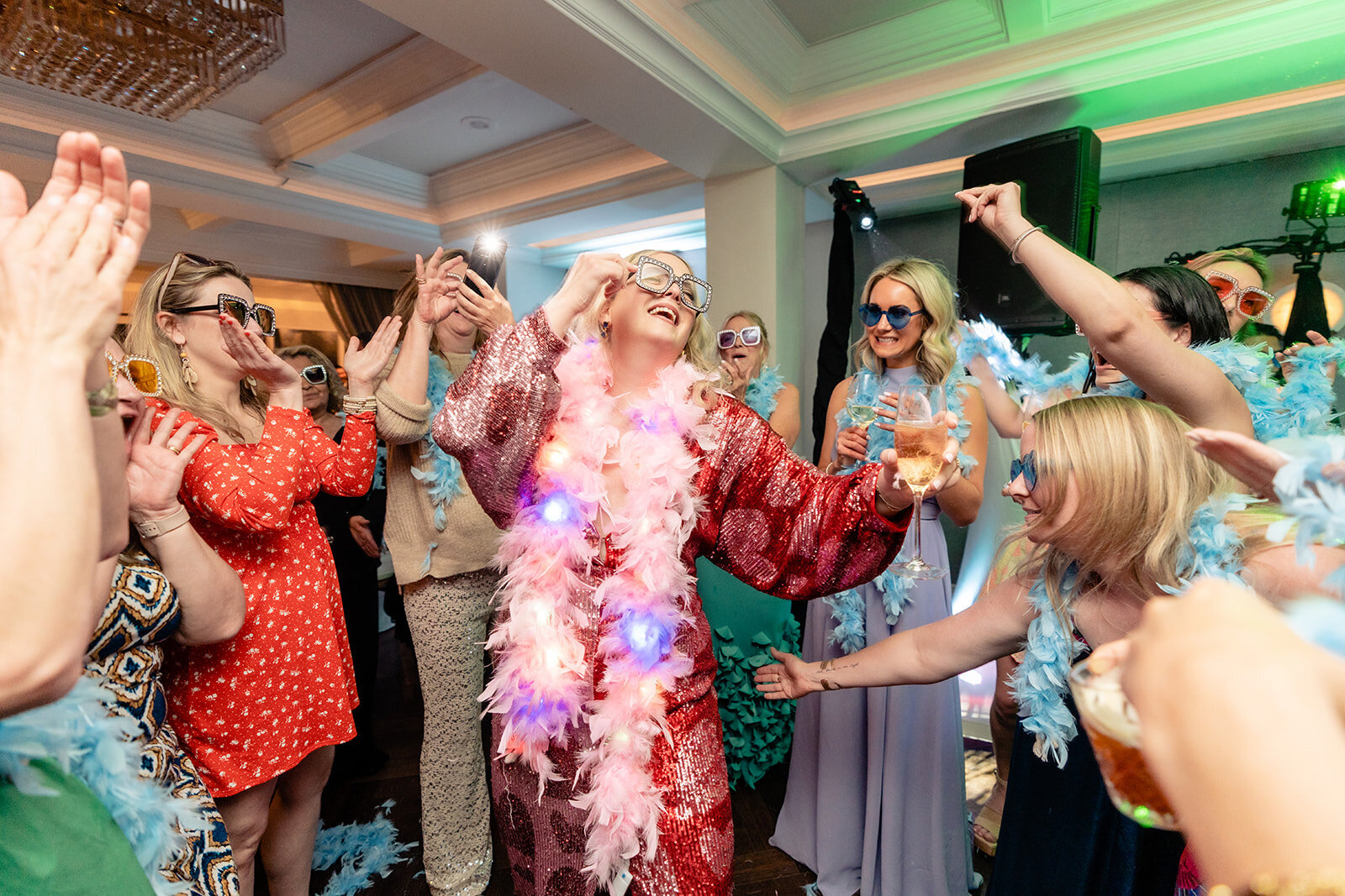 A bride wearing a red heart sequence dress and a pink feather boa surrounded by her girlfriends on the dance floor at La Valencia Hotel