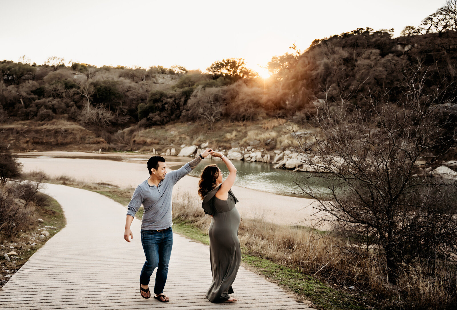 Maternity Photographer, a man dances with his pregnant wife on a paved trail near the lake