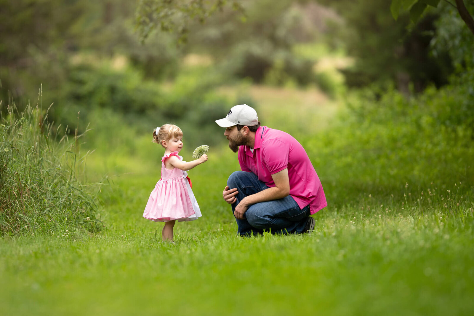 Two year old girl wearing pink dress  is showing her kneeling father a flower