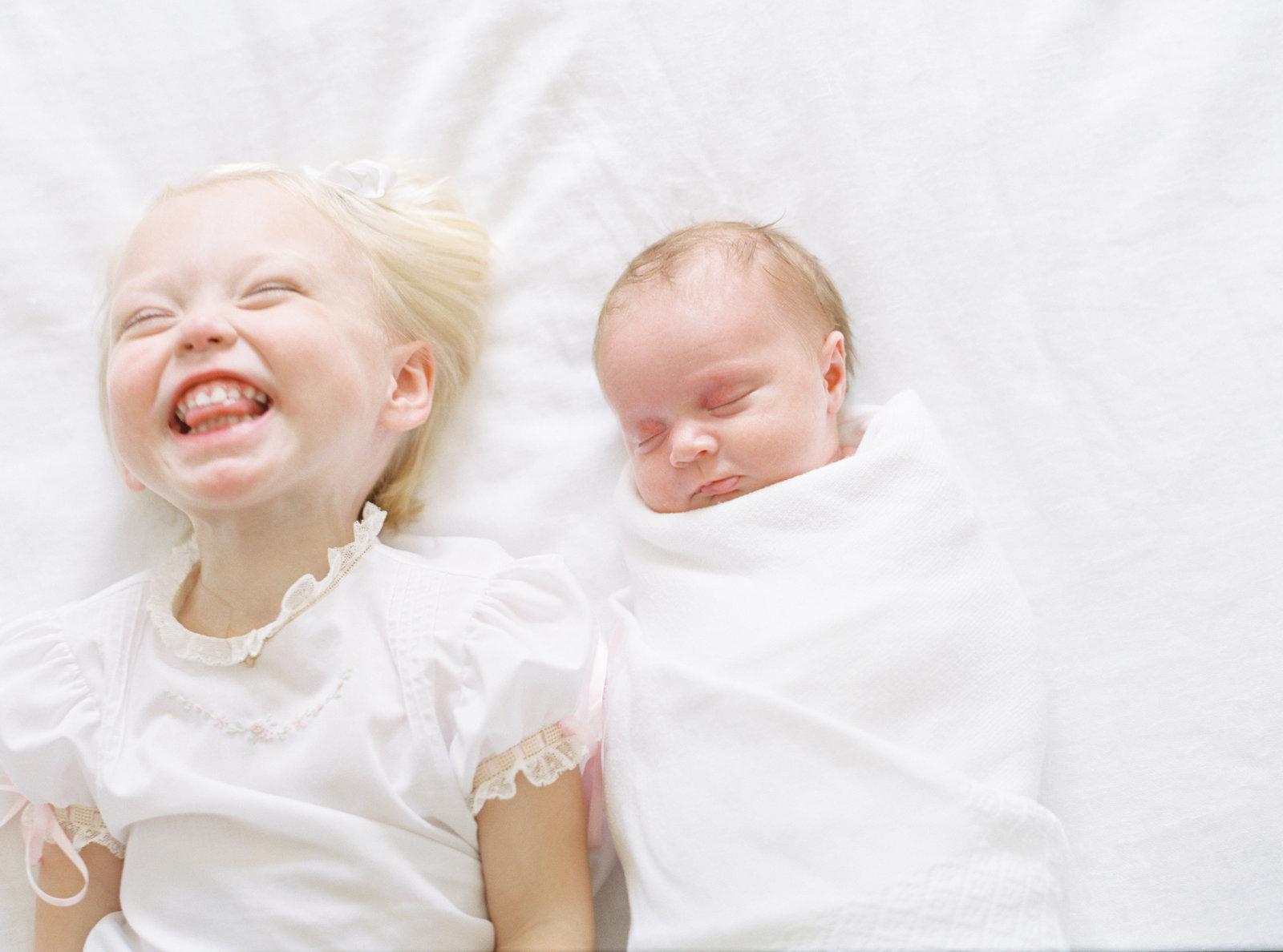 Photograph of a sleeping newborn next to a smiling sister, taken in Birmingham, AL by Alice Claire Photography